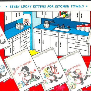 May include: Seven white kitchen towels with colourful embroidered kittens and the text "Good Luck" followed by the day of the week. The towels are displayed in a kitchen setting with white cabinets and a blue countertop.