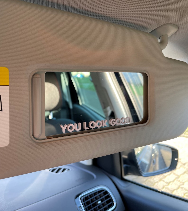 Peut inclure: Une visi&egrave;re pare-soleil de voiture avec un miroir et un autocollant rose qui dit "YOU LOOK GOOD".