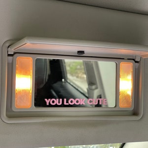 Peut inclure: Un miroir de pare-soleil de voiture avec deux lumi&egrave;res de chaque c&ocirc;t&eacute;. Le miroir a un autocollant rose qui dit "YOU LOOK CUTE".