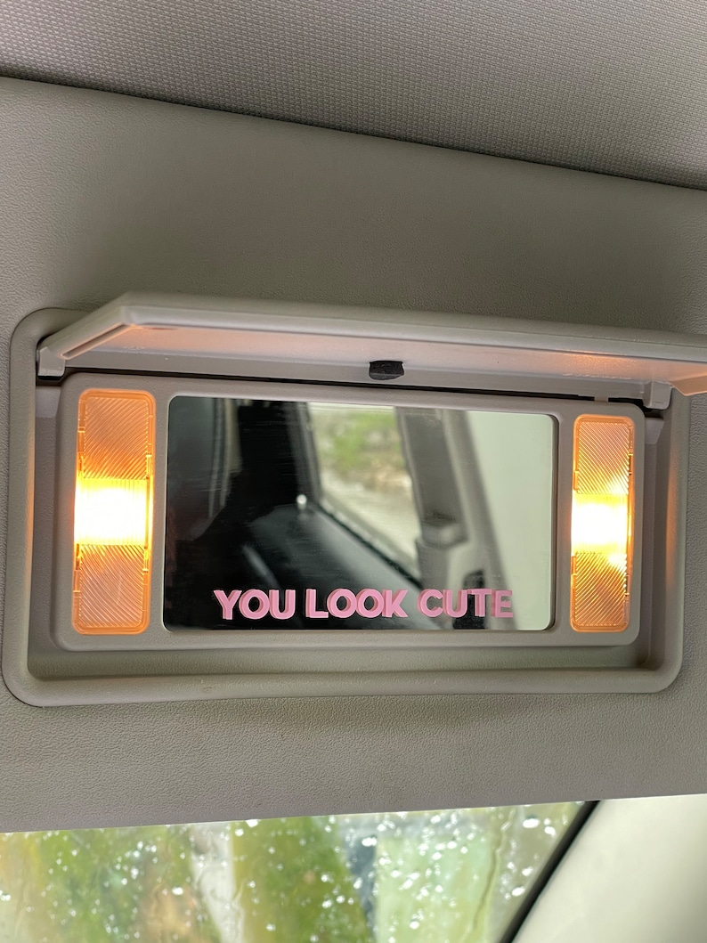Peut inclure: Un miroir de pare-soleil de voiture avec deux lumi&egrave;res de chaque c&ocirc;t&eacute;. Le miroir a un autocollant rose qui dit "YOU LOOK CUTE".