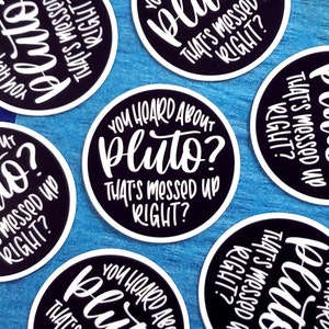 May include: A set of six black and white round stickers with the text "You heard about Pluto? That's messed up right?" The stickers are on a blue wooden surface.