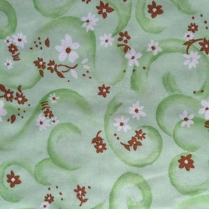 May include: A light green fabric with a repeating pattern of white and brown flowers and green swirls. The flowers have white petals and brown centers, and the swirls are a darker shade of green.