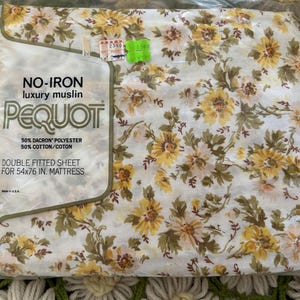 May include: A Pequot double fitted sheet for a 54x76 inch mattress in original plastic packaging. The fabric features a white background with a floral pattern of yellow flowers and green leaves. The label states 50% Dacron polyester and 50% cotton.