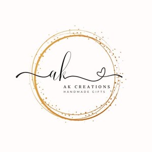 May include: A logo featuring the handwritten letters "ak" in black script, encircled by a gold-colored ring with a dotted texture. The text "AK CREATIONS HANDMADE GIFTS" is below the letters.