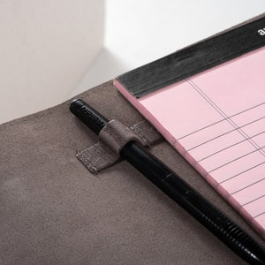 May include: A gray leather notebook with a black pen holder and a pink lined notepad. The notepad has the text "amazonbasics" printed on the cover.