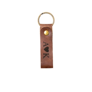 May include: Brown leather keychain with a gold ring and a brass button. The keychain has the letters "A&hearts;K" engraved on it.