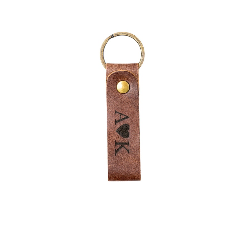 May include: Brown leather keychain with a gold ring and a brass button. The keychain has the letters "A&hearts;K" engraved on it.