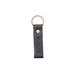 May include: Black leather keychain with a gold ring and a brass button. The keychain has the name "Robert" engraved on it.