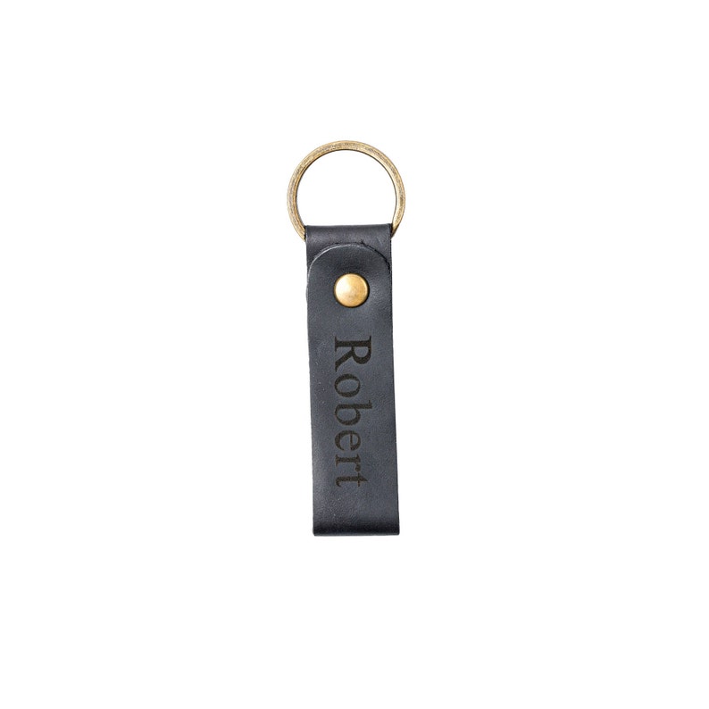 May include: Black leather keychain with a gold ring and a brass button. The keychain has the name "Robert" engraved on it.