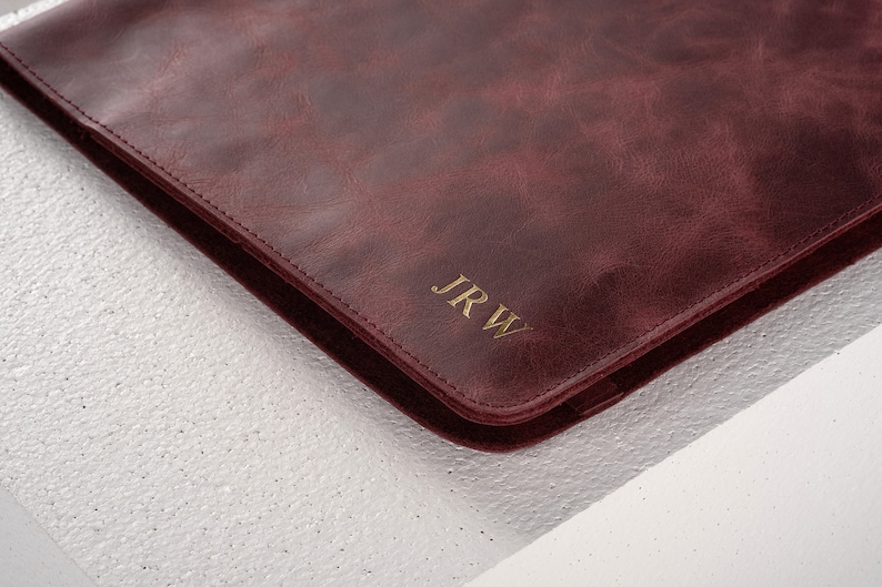 May include: A burgundy leather laptop sleeve with gold embossed initials "JRW".
