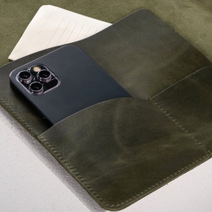 May include: A green leather notebook with a phone and a piece of paper in the pockets.