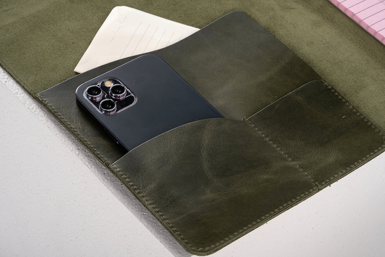 May include: A green leather notebook with a phone and a piece of paper in the pockets.