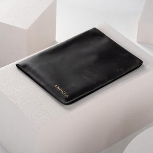 May include: A black leather laptop sleeve with the name "ANDREA" embossed in gold lettering.