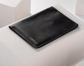 May include: A black leather laptop sleeve with the name "ANDREA" embossed in gold lettering.