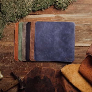 May include: A set of seven leather mousepads in various colors, including brown, green, gray, black, and blue. The blue mousepad has the word "NOVA" printed on it.