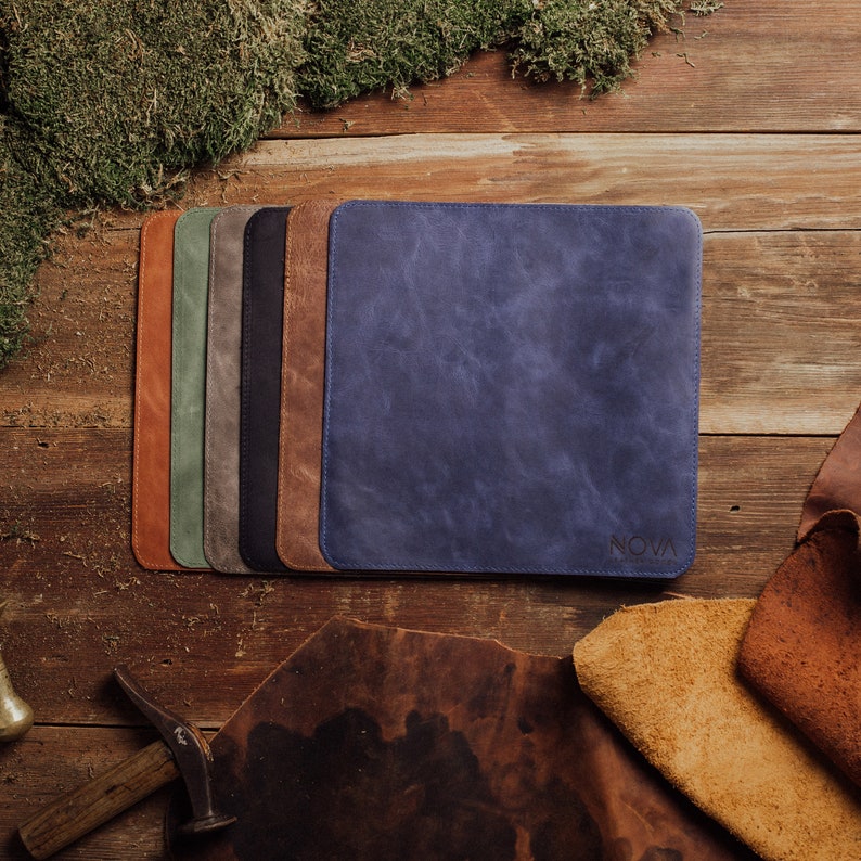 May include: A set of seven leather mousepads in various colors, including brown, green, gray, black, and blue. The blue mousepad has the word "NOVA" printed on it.