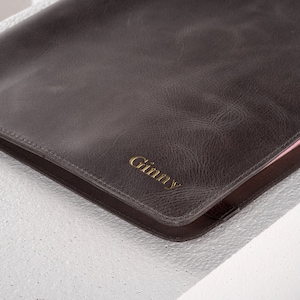 May include: A brown leather folder with a gold embossed name "Ginny" on the front.