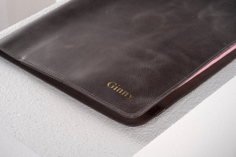 May include: A brown leather folder with a gold embossed name "Ginny" on the front.