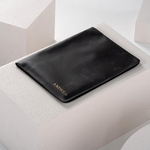 May include: A black leather laptop sleeve with the name "ANDREA" embossed in gold lettering.
