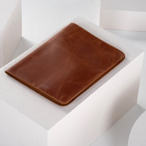 May include: A brown leather laptop sleeve with a subtle embossed logo.