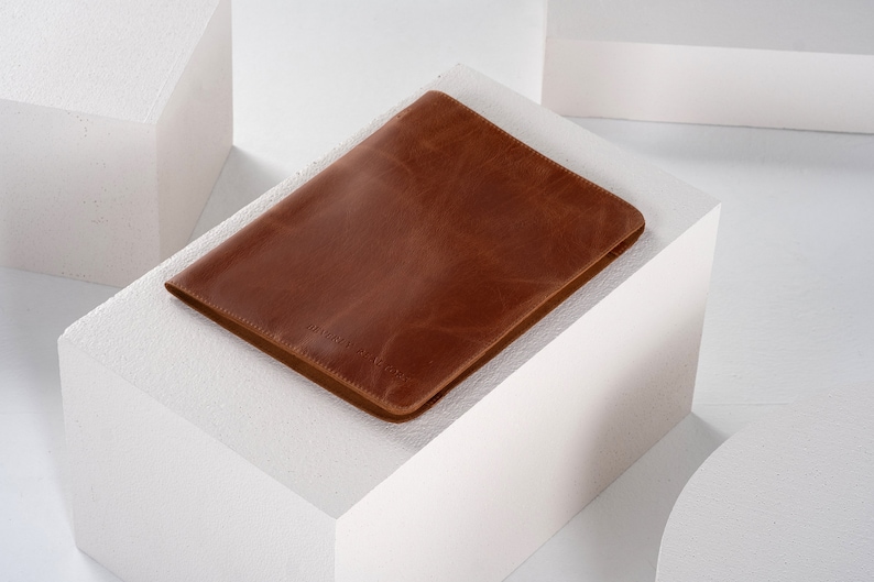 May include: A brown leather laptop sleeve with a subtle embossed logo.