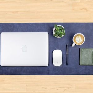 May include: A blue leather desk mat with a laptop, mouse, pen, coffee cup, and a small potted plant.