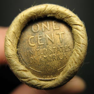 Puede incluir: Primer plano de un rollo de centavos. El extremo del rollo muestra un centavo de color cobre con las palabras "ONE CENT" y "UNITED STATES OF AMERICA". El rollo de papel es de color beige y tiene un aspecto texturizado y tejido.