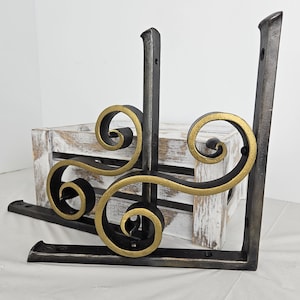 May include: Two decorative metal shelf brackets. The brackets are black with gold scrollwork accents. The brackets are made of metal and have a sturdy design. The brackets are designed to be mounted on a wall and support a shelf.