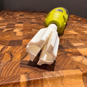 May include: A close-up of a white immersion blender attachment with a yellow and black handle. The attachment has a star-shaped design with multiple blades.