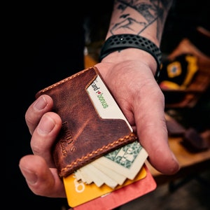 May include: A brown leather wallet with visible stitching and multiple card slots. The wallet is filled with cards and cash, including a card that says "card bonus". The wallet has the text "FAMILY'S house" on the front.