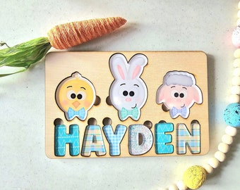 May include: Wooden puzzle with three characters: a chick, a bunny, and a sheep. Each character has a blue bow tie. The puzzle pieces are shaped like the characters and fit into the wooden board. The name "HAYDEN" is spelled out in blue and white checkered letters on the board.