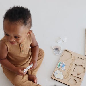 May include: A wooden puzzle with colorful illustrations of religious symbols. The puzzle pieces are shaped like the symbols and fit into the corresponding cutouts on the board. The text on the board reads "Jesus Loves Little Lambs".