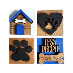 May include: Four wooden dog-themed decorations. One features a dog house with a blue roof and door, and a bone. Another has a black paw print inside a heart. The third has a black paw print. The last says "LESS PEOPLE more dogs" with a bone.