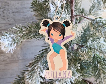 Op de afbeelding: Een houten kerstversiering met een cartoon-gymnast in een paars en turquoise pakje. De versiering is gepersonaliseerd met de naam "JULIANA".