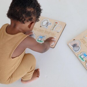 May include: A child plays with a wooden puzzle set featuring images of religious symbols. The puzzle pieces are labeled "Jesus Loves Little Kids" and "Jesus Loves Ellington".