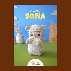 May include: A crocheted sheep toy with the name "SOFIA" in yellow text. The sheep is white with pink accents on its cheeks and ears. The background is a blue sky with clouds and a green field.