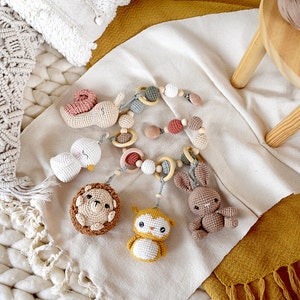 May include: A handmade crochet baby mobile featuring various animal shapes, including a snail, duck, hedgehog, owl, and bunny. The mobile includes wooden rings and beads, with a neutral color palette of white, brown, and pastel accents.