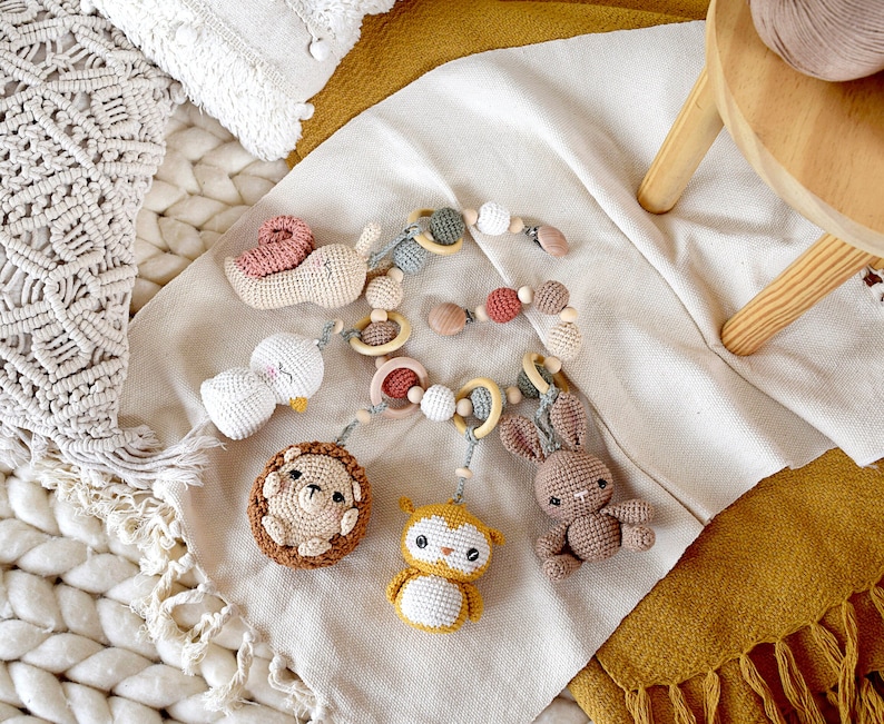 May include: A handmade crochet baby mobile featuring various animal shapes, including a snail, duck, hedgehog, owl, and bunny. The mobile includes wooden rings and beads, with a neutral color palette of white, brown, and pastel accents.