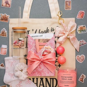 Puede incluir: Un bolso tote beige con asas color crema, lleno de una caja de regalo rosa con estampado floral, un tarro de cristal, una vela y otros accesorios. El bolso tote tiene la palabra "HAND" impresa. Tambi&eacute;n se incluyen pegatinas y un lazo rosa.