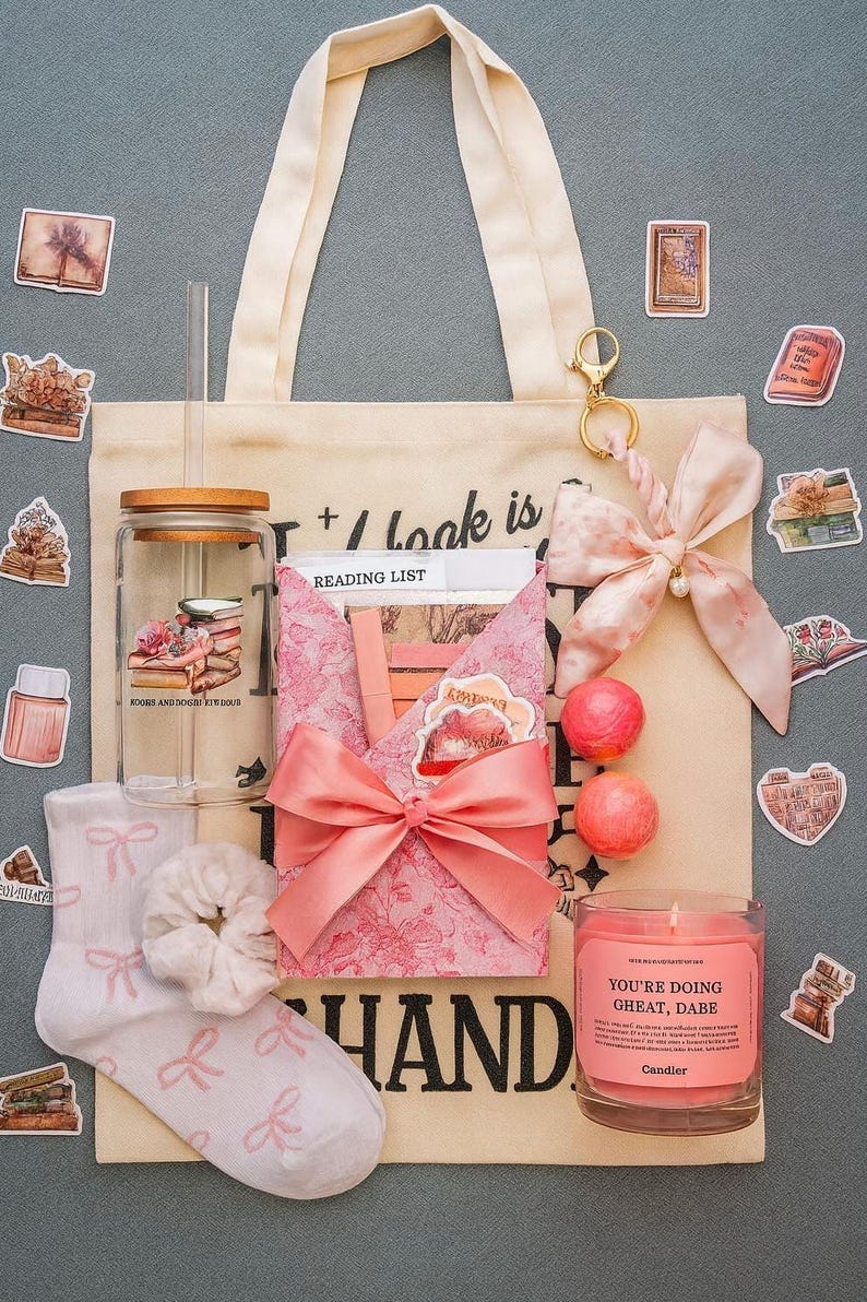 Puede incluir: Un bolso tote beige con asas color crema, lleno de una caja de regalo rosa con estampado floral, un tarro de cristal, una vela y otros accesorios. El bolso tote tiene la palabra "HAND" impresa. Tambi&eacute;n se incluyen pegatinas y un lazo rosa.
