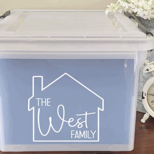 May include: A clear plastic storage bin with a blue label that says "The West Family" in a white stylized font with a house graphic.