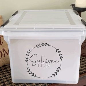 May include: A clear plastic storage bin with a black lid and a black and white vinyl sticker that says "Sullivan Est. 2021" with a wreath design.