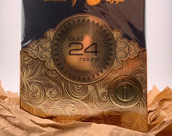 May include: A black and gold box with Arabic text and the words "oud 24 hours" in a circle. The box is wrapped in brown paper.