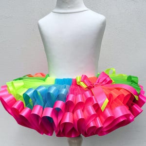 May include: A colorful tutu skirt with multiple layers of neon pink, blue, green, and yellow ribbon. The skirt is on a white mannequin.