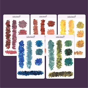 Op de afbeelding: Een verzameling aquarelstickervellen met verschillende kleurenpaletten. Elke vel toont penseelstreken en spatten in tinten rood, bruin, blauw, groen en geel. De tekst "julia here" staat op elk vel.