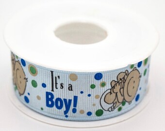 May include: A spool of light blue ribbon printed with "It's a Boy!" in blue and black. The ribbon design includes a cartoon baby and polka dots in blue, green, and tan.