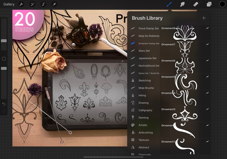 May include: A digital drawing tablet with a stylus and a selection of 20 decorative stamps displayed on the screen. The stamps are black and white and feature various floral and geometric designs. The tablet is on a wooden surface with a tattoo machine and other tools.