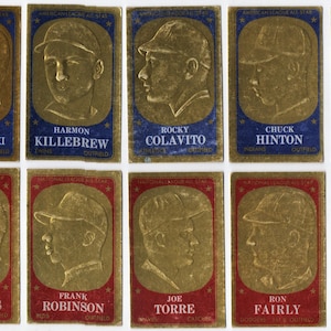 May include: A collection of vintage baseball cards featuring gold-toned portraits of baseball players. Each card has a colored border and the player's name and team information. The cards are arranged in rows and columns.