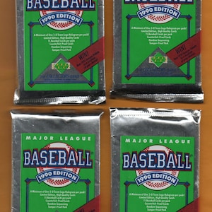 May include: Four sealed baseball card packs from the 1990 edition. Each pack features a green and white design with the word "BASEBALL" prominently displayed. The packs are sealed in silver foil.