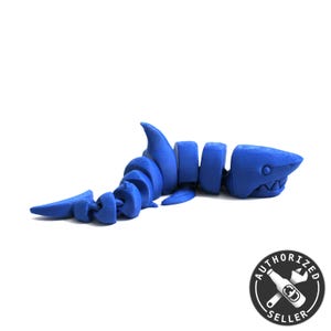 Könnte beinhalten: Ein blaues 3D-gedrucktes Hai-Skelettmodell. Das Modell besteht aus segmentierten Teilen, die miteinander verbunden sind. Der Hai hat eine realistische Form und Merkmale, darunter einen Mund mit Zähnen.